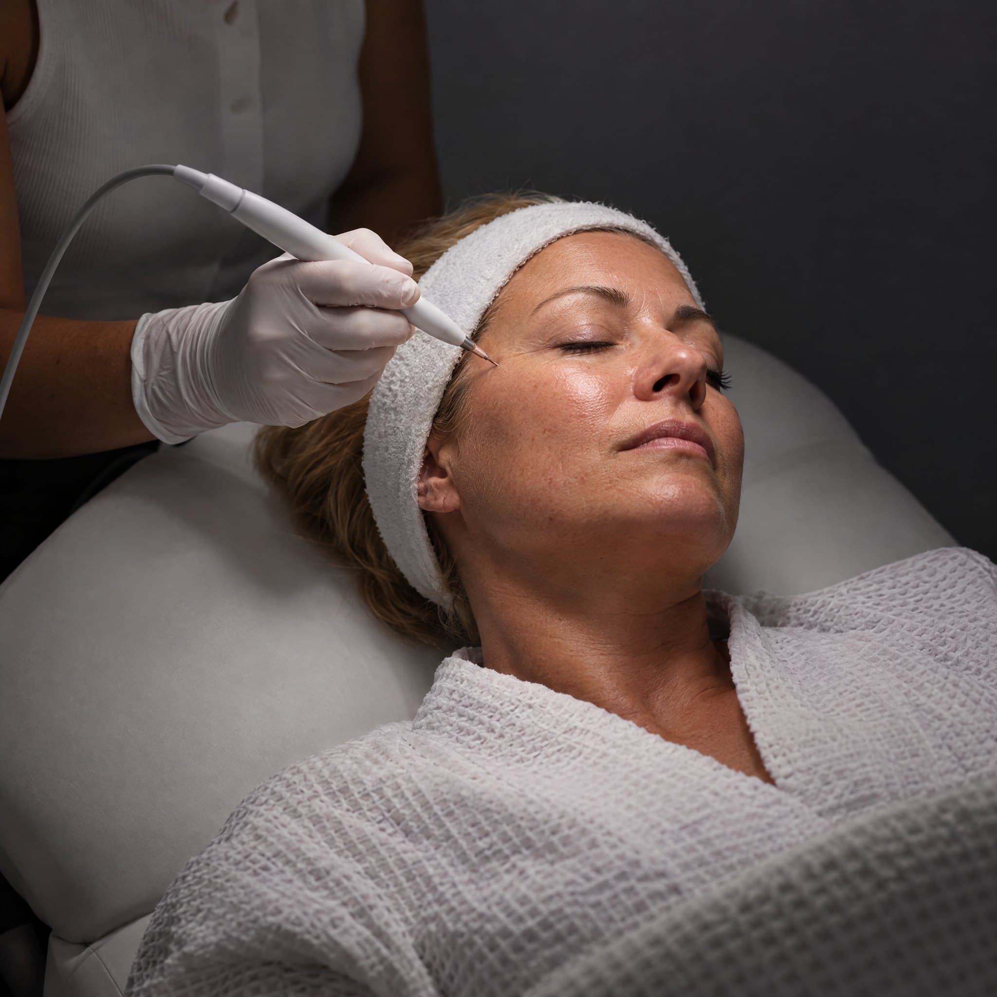 An Ora provider guiding a resurfacing handpiece along a client's cheek