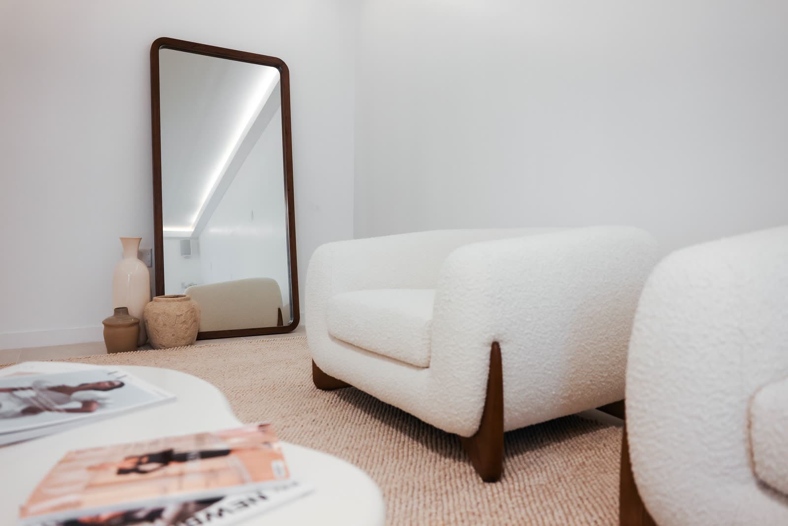 A boucle lounge chair beside a full-length walnut mirror at Ora