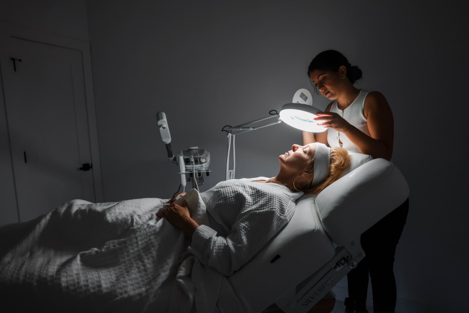 A facial treatment in progress under a lighted lamp at Ora