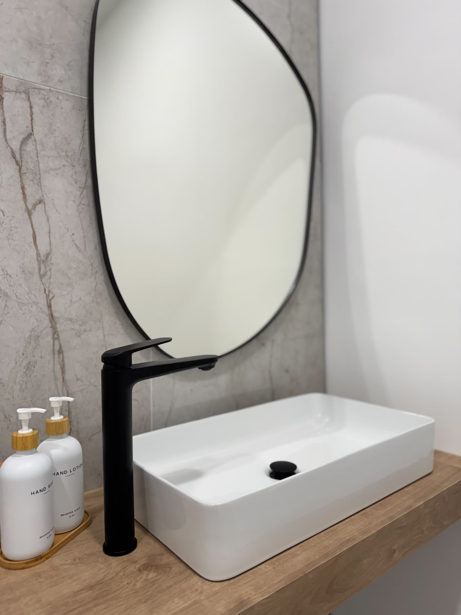 A washroom vanity at Ora — a vessel sink and black faucet on a wood shelf, under a pebble-shaped mirror